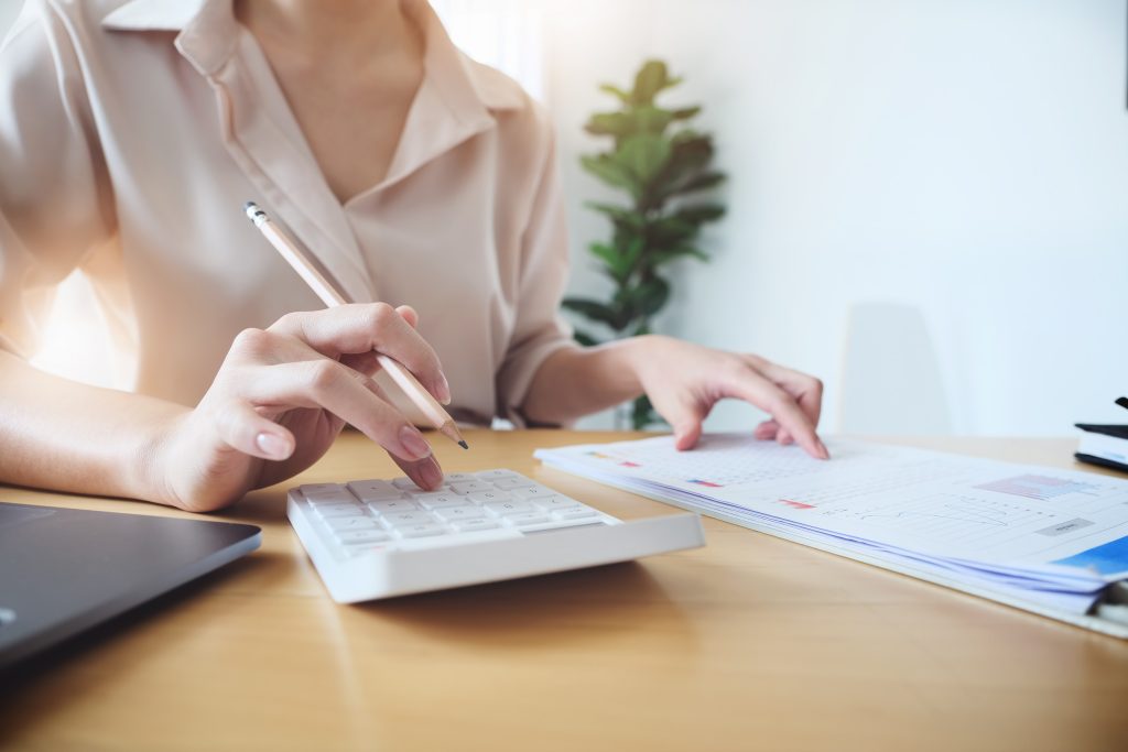 Business woman using calculator to review balance sheet annual using document and laptop computer to calculating budget. audit and Check integrity before investment concept